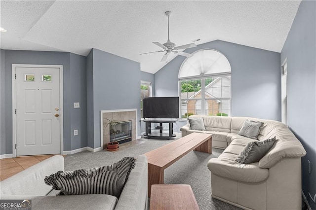 living room featuring vaulted ceiling, tile patterned flooring, ceiling fan, a textured ceiling, and a tiled fireplace