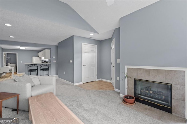 carpeted living room with a tiled fireplace and vaulted ceiling