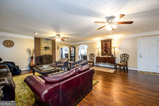 living room featuring ceiling fan, a brick fireplace, dark wood-type flooring, a textured ceiling, and ornamental molding