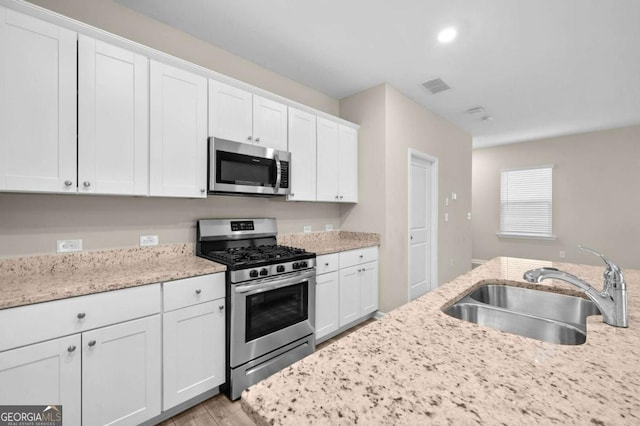 kitchen with white cabinets, sink, light hardwood / wood-style flooring, light stone countertops, and appliances with stainless steel finishes