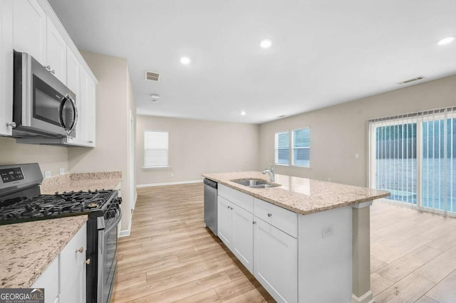 kitchen with light stone countertops, sink, a kitchen island with sink, white cabinets, and appliances with stainless steel finishes