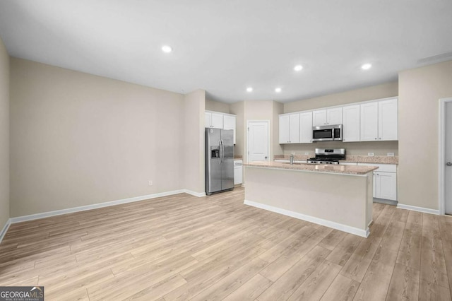 kitchen featuring stainless steel appliances, light stone counters, light hardwood / wood-style flooring, an island with sink, and white cabinets