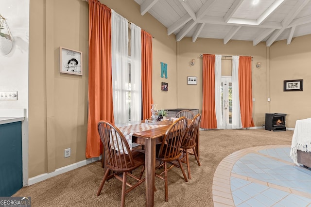 dining space with beamed ceiling, a wood stove, carpet floors, and wooden ceiling