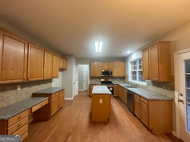 kitchen with sink, light wood-type flooring, appliances with stainless steel finishes, tasteful backsplash, and a kitchen island