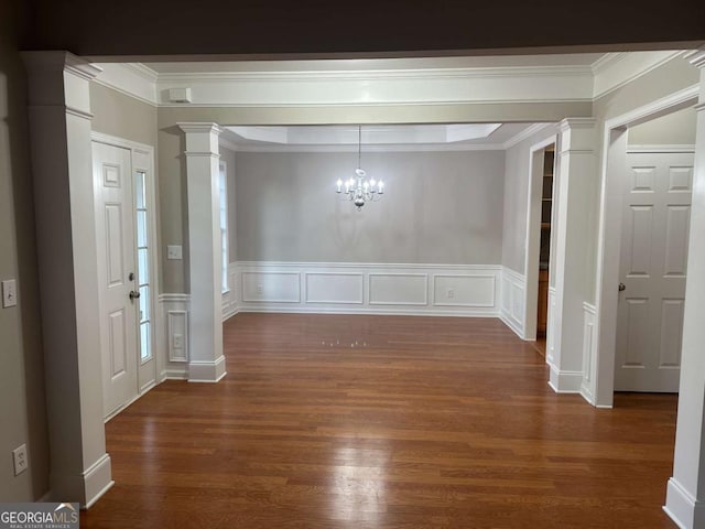 unfurnished dining area featuring dark hardwood / wood-style floors, an inviting chandelier, ornamental molding, and ornate columns