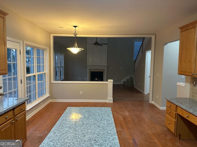 kitchen featuring a large fireplace, decorative light fixtures, ceiling fan, and dark wood-type flooring