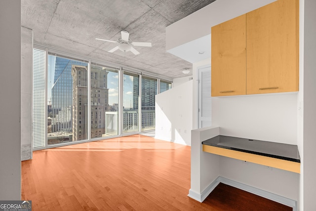 interior space with ceiling fan, floor to ceiling windows, built in desk, and light wood-type flooring