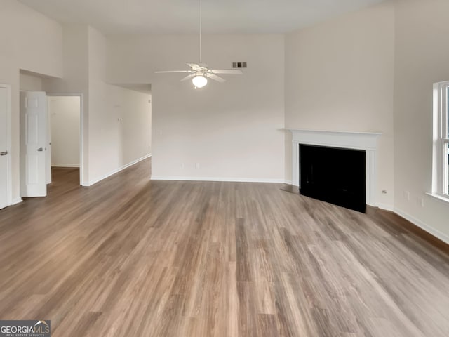 unfurnished living room featuring hardwood / wood-style floors, ceiling fan, and a high ceiling