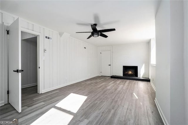 unfurnished living room with hardwood / wood-style flooring, ceiling fan, and a large fireplace