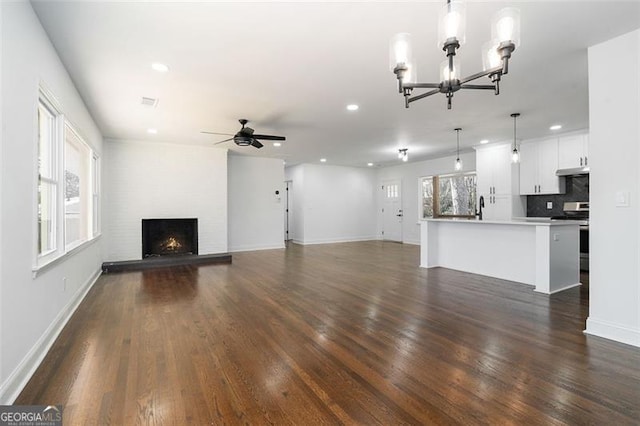 unfurnished living room with sink, ceiling fan with notable chandelier, dark hardwood / wood-style flooring, and a fireplace