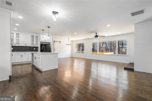 kitchen featuring a kitchen island with sink, white cabinets, decorative backsplash, ceiling fan, and decorative light fixtures