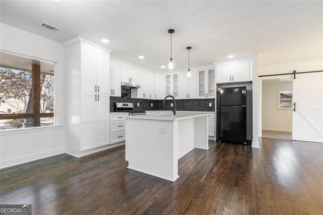 kitchen with hanging light fixtures, a barn door, black fridge, a kitchen island with sink, and stainless steel stove