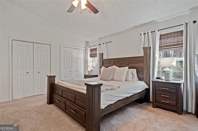 bedroom featuring light carpet, a textured ceiling, vaulted ceiling, ceiling fan, and multiple closets