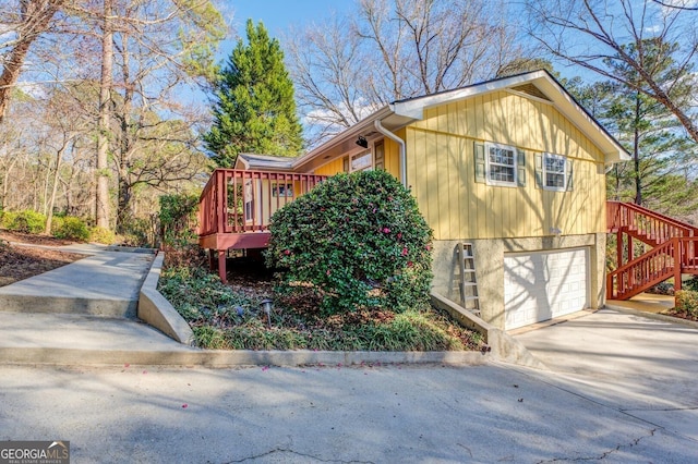 view of side of home with driveway, an attached garage, stairway, and a deck