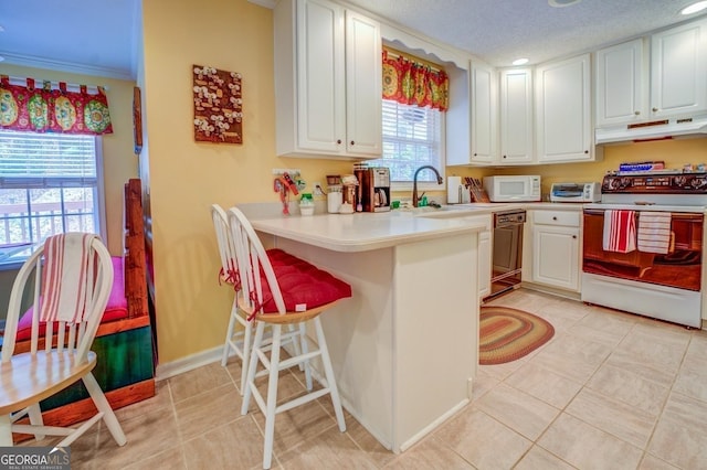 kitchen featuring under cabinet range hood, a breakfast bar, a sink, light tile patterned floors, and white appliances