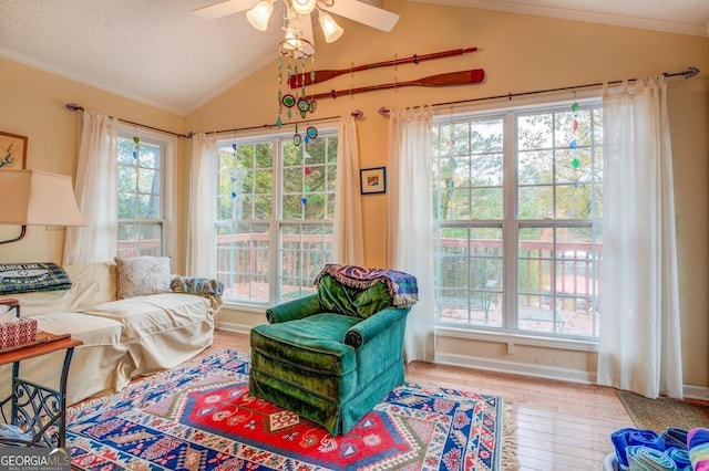 living area featuring lofted ceiling, wood finished floors, ornamental molding, baseboards, and ceiling fan
