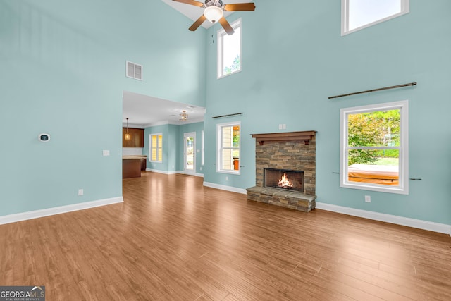 unfurnished living room with a stone fireplace, ceiling fan, hardwood / wood-style floors, and a high ceiling