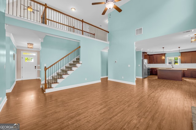 unfurnished living room featuring ornamental molding, ceiling fan, dark wood-type flooring, sink, and a high ceiling