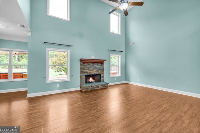 unfurnished living room with a towering ceiling, a stone fireplace, a wealth of natural light, and ceiling fan