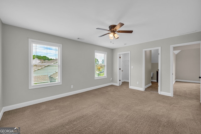 unfurnished bedroom with light carpet, connected bathroom, a spacious closet, and ceiling fan