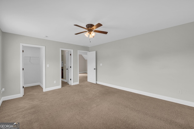 unfurnished bedroom with a walk in closet, a closet, ceiling fan, and light colored carpet