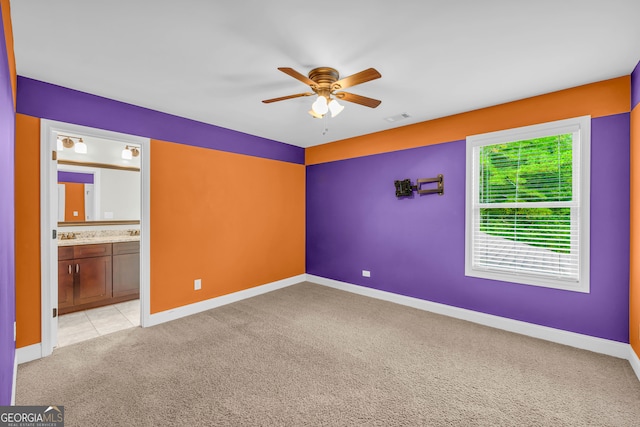 unfurnished bedroom with ceiling fan, ensuite bathroom, and light carpet