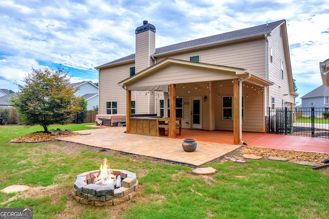 rear view of property featuring a fire pit, a bar, a patio, and a lawn