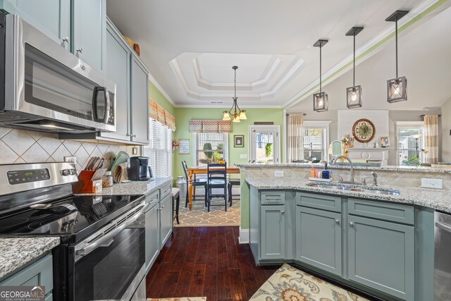 kitchen featuring appliances with stainless steel finishes, dark hardwood / wood-style flooring, a tray ceiling, sink, and hanging light fixtures