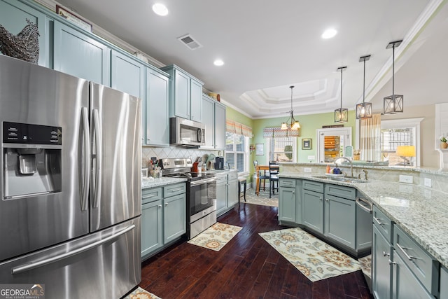 kitchen featuring sink, an inviting chandelier, pendant lighting, a tray ceiling, and appliances with stainless steel finishes