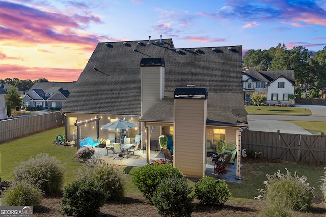 back house at dusk featuring a lawn and a patio