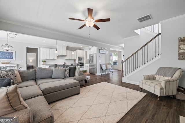 living room featuring wood-type flooring, ceiling fan with notable chandelier, and ornamental molding