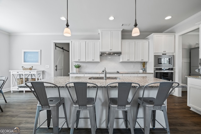 kitchen with stainless steel appliances, sink, pendant lighting, a barn door, and white cabinets