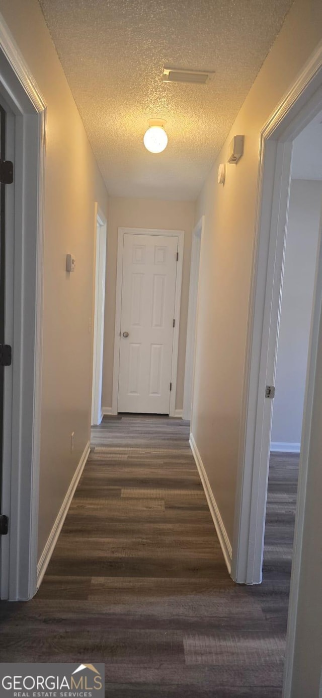 hallway with a textured ceiling and dark hardwood / wood-style floors