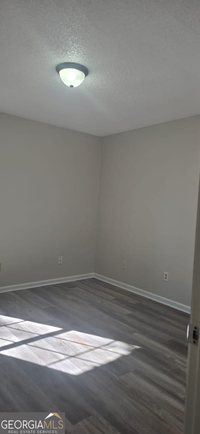 empty room with a textured ceiling and dark hardwood / wood-style flooring