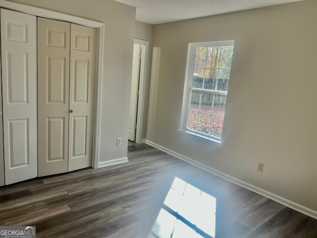 unfurnished bedroom featuring a closet, dark hardwood / wood-style floors, and multiple windows