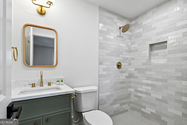 bathroom featuring vanity, a tile shower, and toilet