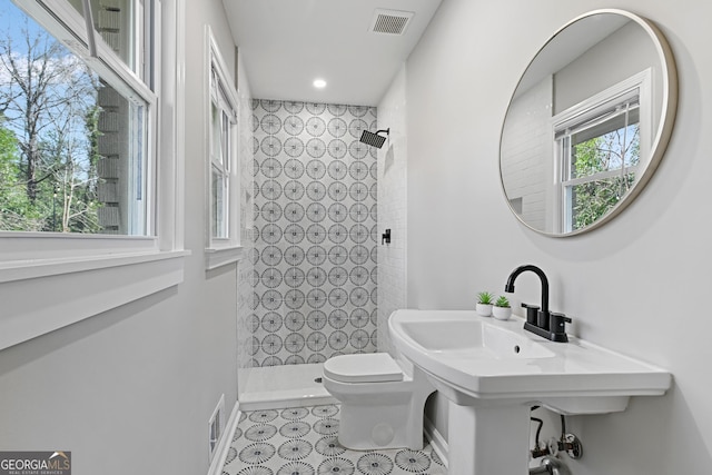 bathroom with tiled shower, toilet, and a wealth of natural light