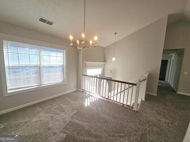 spare room featuring a chandelier, a textured ceiling, carpet floors, and vaulted ceiling