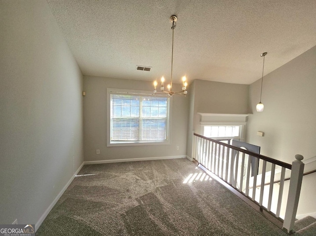 carpeted empty room featuring a textured ceiling and a notable chandelier