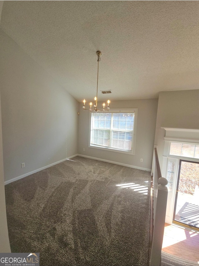 carpeted spare room featuring a textured ceiling and an inviting chandelier