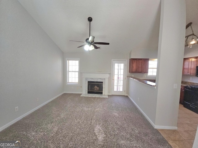 unfurnished living room featuring vaulted ceiling, ceiling fan, a healthy amount of sunlight, and a premium fireplace