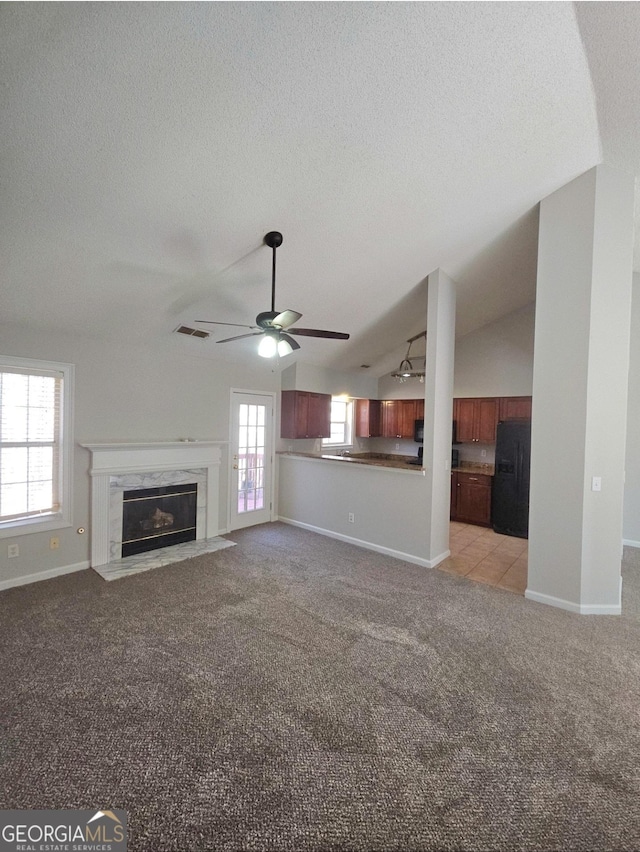 unfurnished living room with ceiling fan, light colored carpet, a textured ceiling, lofted ceiling, and a fireplace