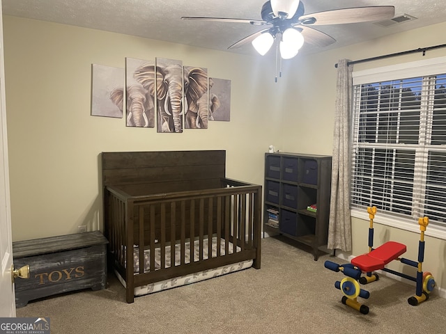 bedroom featuring carpet flooring, ceiling fan, a nursery area, and a textured ceiling