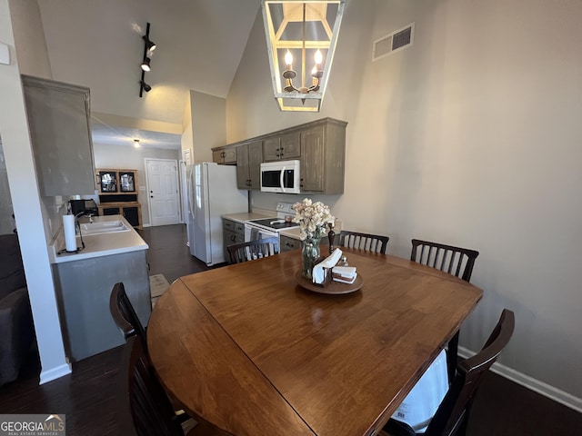 dining room featuring high vaulted ceiling, track lighting, sink, dark hardwood / wood-style floors, and a notable chandelier