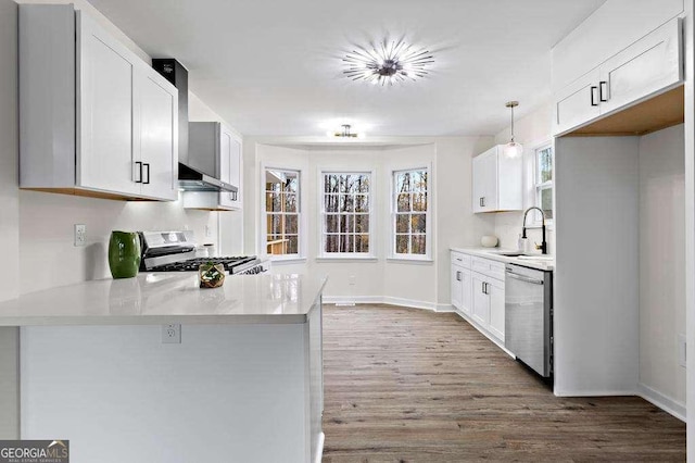 kitchen featuring white cabinetry, sink, stainless steel appliances, wall chimney range hood, and decorative light fixtures