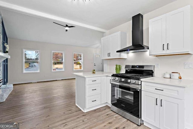 kitchen featuring kitchen peninsula, light wood-type flooring, wall chimney range hood, white cabinets, and stainless steel range with gas stovetop