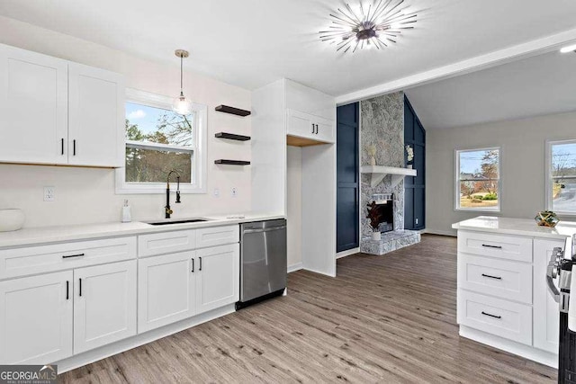 kitchen featuring stainless steel dishwasher, sink, decorative light fixtures, white cabinetry, and a stone fireplace