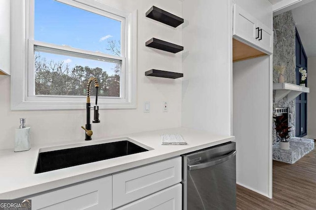 kitchen featuring dishwasher, dark wood-type flooring, sink, a fireplace, and white cabinetry