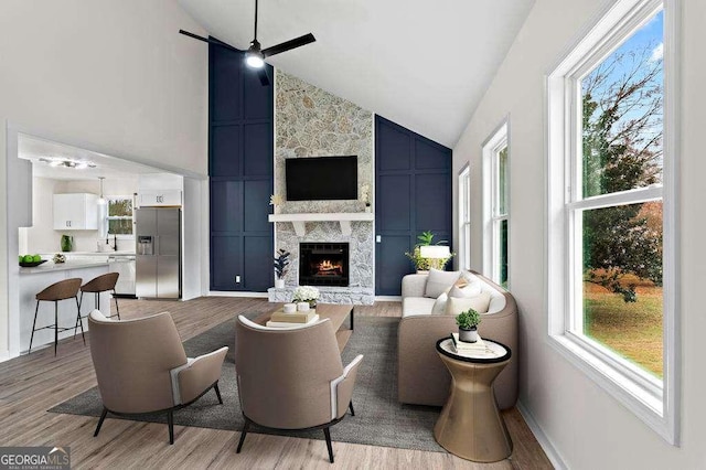 living room featuring ceiling fan, a large fireplace, a healthy amount of sunlight, and light wood-type flooring