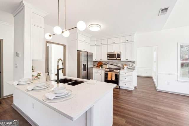 kitchen with appliances with stainless steel finishes, light stone counters, sink, pendant lighting, and white cabinets